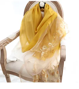 Detail of yellow silk wool shawl featuring intricate gold floral embroidery on vintage wood