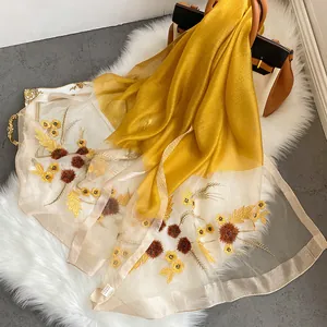 Detailed close-up of ginger yellow silk wool scarf with floral embroidery and 3D pom-poms