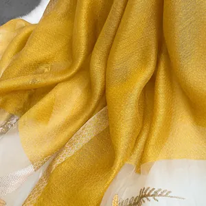 Detailed close-up of golden silk wool shawl featuring intricate leaf embroidery and fringes