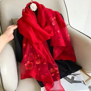 Detailed close-up of red silk wool scarf featuring intricate floral embroidery and camellia
