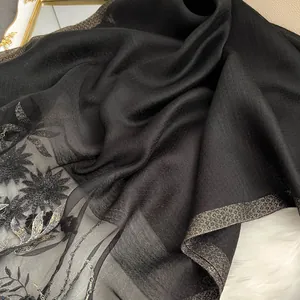 Close-up of black silk wool scarf with intricate floral embroidery and shimmering trim