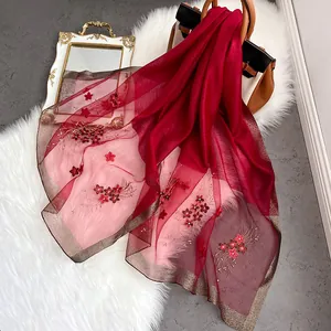 Détail macro d'une écharpe en soie rouge avec broderie florale et sequins brillants