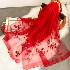 Détail d'une écharpe en soie rouge avec broderie de fleurs de prunier et texture légère