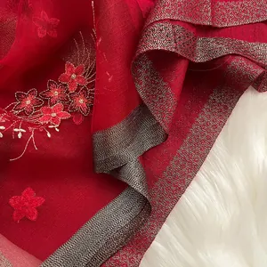 Détail d'un châle en soie rouge avec broderie florale et bordure tissée métallique