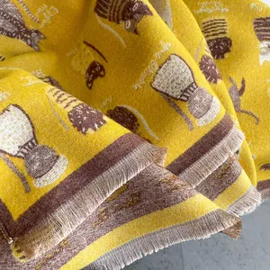 Detail of yellow knit scarf showing cute woven cat patterns and fringe texture