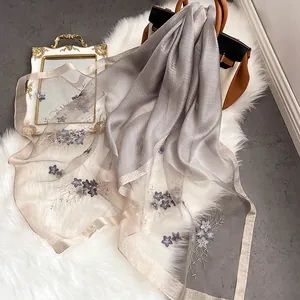 Écharpe longue en soie grise avec broderies florales mauves sur tapis en peluche