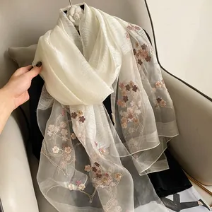 Détail d'une écharpe en soie et laine crème avec broderie florale et broche camélia