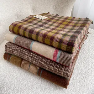 Detail of four plaid cashmere scarves stacked on a white fleece chair showing soft textures