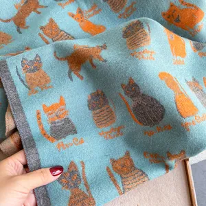 Detail of soft blue knit scarf featuring cute orange cat patterns and artistic script