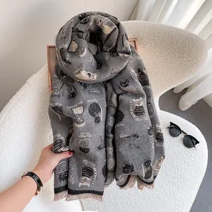 Gray knitted scarf with cartoon cat patterns and fine fringe on a cozy white sofa