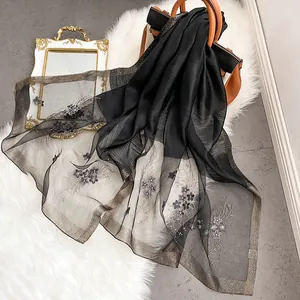 Détail d'une écharpe en soie noire transparente avec bordure dorée et broderie florale