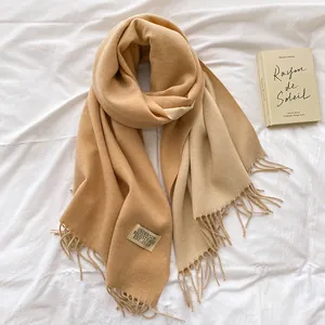 Close-up of beige gradient cashmere-like scarf with fringe edges and logo tag