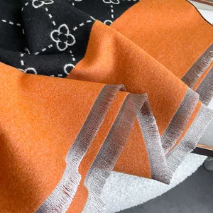 Detail of cashmere-like scarf showing black and orange floral patterns with fringe