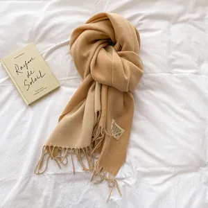 Solid camel cashmere-like scarf with fringe and woven label on a minimalist background