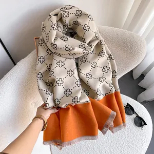 Detail of cashmere-like scarf showing beige clover patterns with orange block and grey fringes
