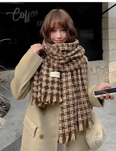 Close-up of brown houndstooth scarf with tassels on a model wearing khaki wool coat