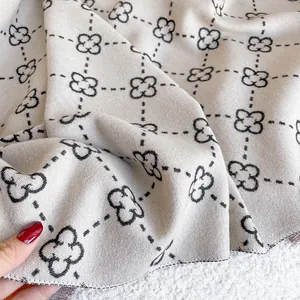 Macro view of oatmeal cashmere scarf with black four-leaf clover pattern and fine texture