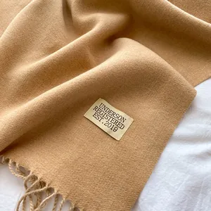 Close-up of caramel cashmere-feel scarf showing soft texture, fringe, and brand label