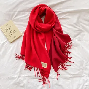 Detail of red cashmere-feel scarf with fine fringe tassels and beige brand woven label