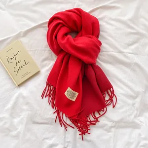 Detailed view of a red cashmere-feel scarf with fringe tassels and a woven brand label