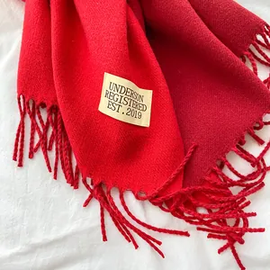 Detail of red faux cashmere scarf featuring a sewn-on label and long tassel edges