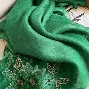Broderie détaillée avec motifs floraux verts et perles cousues sur un châle en soie