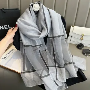 Détail d'une écharpe en soie à carreaux légère avec décoration de camélia blanc