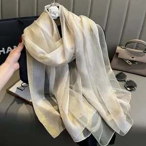 Détail d'une écharpe en soie avec rayures dorées et texture de tissu beige léger