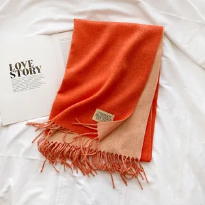 Detail of double-sided cashmere scarf in orange and beige with fringe and woven label