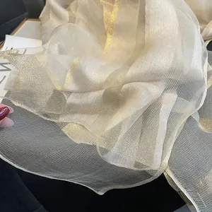 Détail d'une écharpe en soie champagne montrant la texture plissée et le fil métallique doré