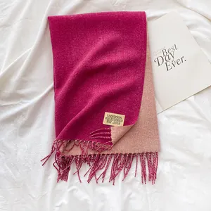 Close-up of double-sided cashmere-like scarf with fringe and brand label on white fabric