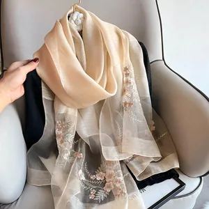 Close-up of silk wool scarf featuring delicate floral embroidery on champagne fabric