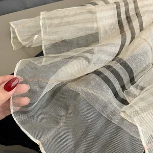 Detail of sheer silk scarf showing brown and orange plaid pattern and fine pleats