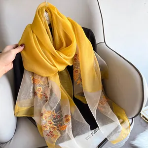 Detail of yellow silk wool scarf featuring intricate orange flower embroidery on hem