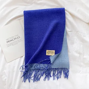 Detailed close-up of double-sided blue cashmere-like scarf with fringe and brand label