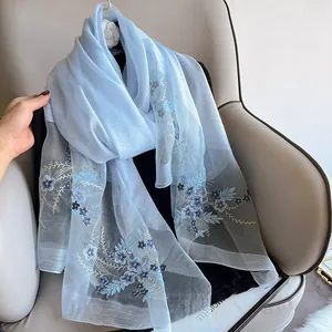 Detailed embroidery of light blue flowers on sheer silk wool scarf draped over a chair