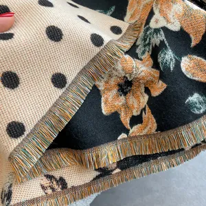 Detail view of double-sided knit scarf showing black polka dots and orange floral patterns
