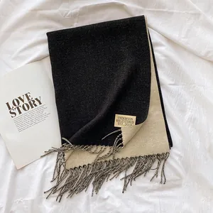 Close-up of dual-sided knit scarf in black and beige with fringe and brand label detail