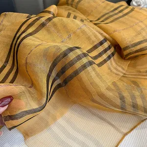 Detailed macro shot of orange silk scarf showing sheer texture and metallic gold stripes