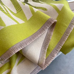 Dettaglio dello scialle in maglia jacquard verde lime e bianco sporco con nappe e motivi