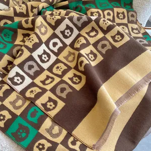 Détail d'une écharpe en maille épaisse avec motifs de chats, damier et franges