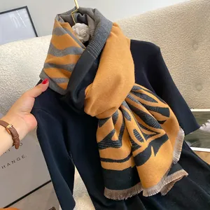 Dettaglio di una spessa sciarpa giallo senape e grigia con motivo zebra e piccole frange