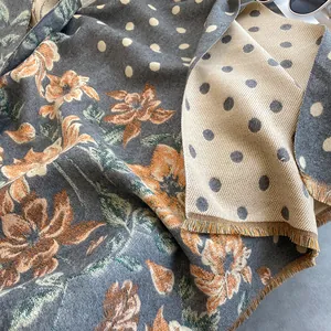 Close-up of thick floral jacquard scarf featuring grey base, orange flowers and tassels