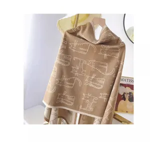 Détail d'une écharpe marron aux motifs de chats blancs et franges sur un cintre en bois