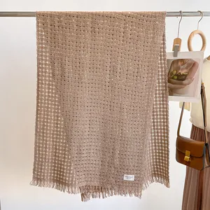 Detail van bruine opengewerkte wollen sjaal met franjes en een boutique-merklabel