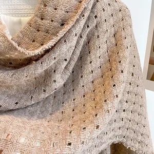 Detailopname van de opengewerkte gebreide textuur en franje van een beige wollen sjaal