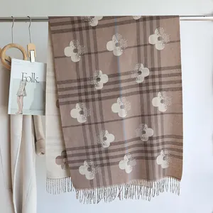 Detail of plaid faux cashmere scarf with flower print and fringe on a metal rack