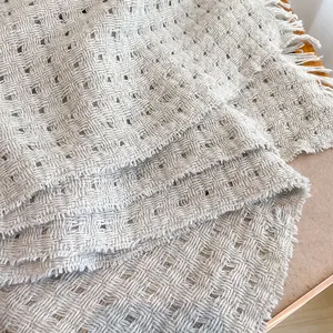 Detailopname van beige wollen sjaal met opengewerkte roostertextuur en fijne franjes