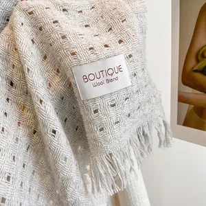 Detailopname van de lichtgrijze wolmix sjaal met opengewerkt breisel en het boutique-label