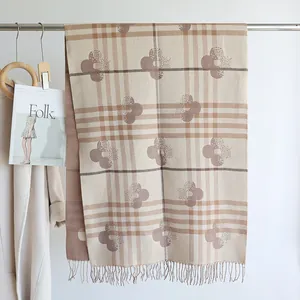 Detail view of beige and brown plaid cashmere-like scarf with fringe and clover print
